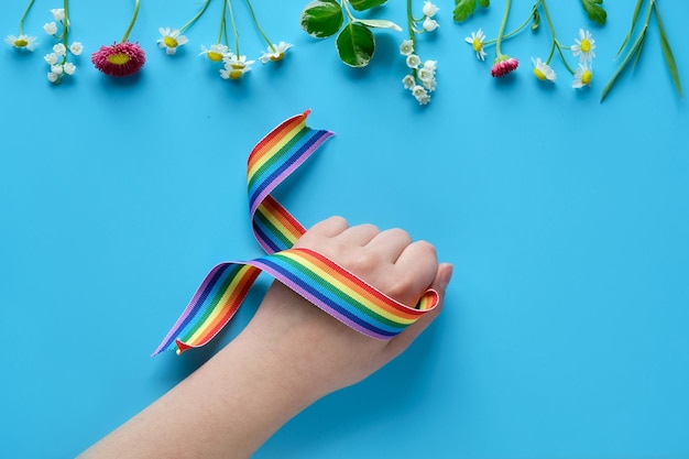 Nastro arcobaleno in mano di bambino sfondo di carta blu menta con fiori selvatici