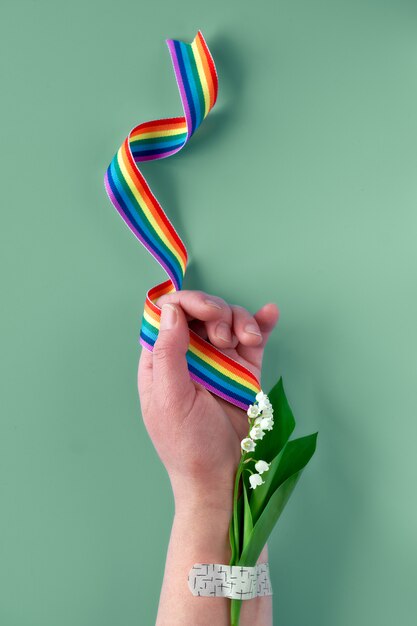 Nastro arcobaleno in mano di donna matura con fiori di mughetto. Bouquet attaccato con cerotto per assistenza medica. Grazie medici e infermieri del SSN!