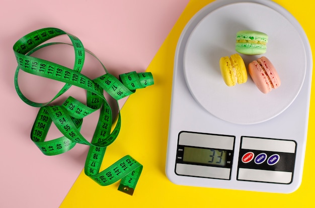 Nastro di misurazione verde, bilancia da cucina digitale con macarons su giallo e rosa. Nessun giorno di dieta