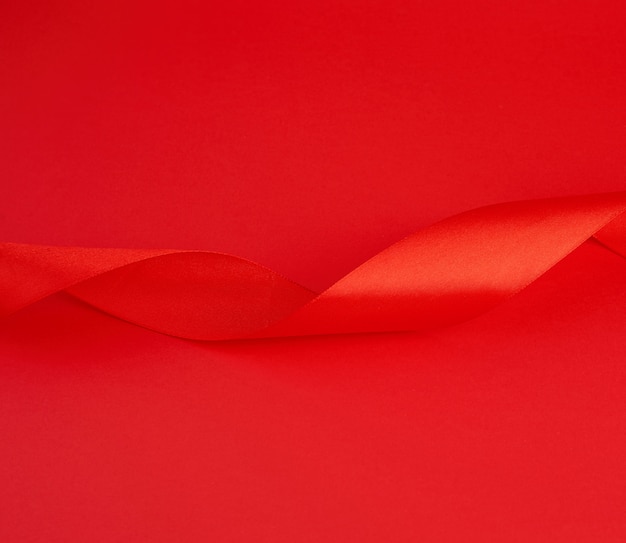 Nastro lucido di seta rosso torto su una priorità bassa rossa, elemento festivo di disegno