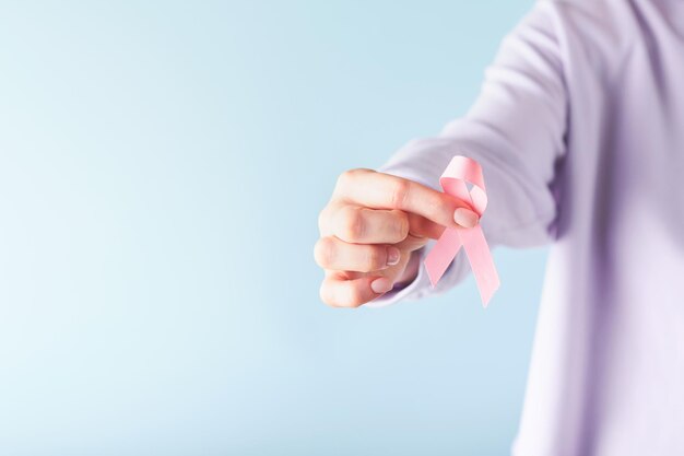 Nastro rosa per la consapevolezza del cancro al seno Mani femminili che tengono un nastro rosa su sfondi blu Consapevolezza del cancro al seno e giornata rosa di ottobre Giornata mondiale del cancro Vista dall'alto Mock up