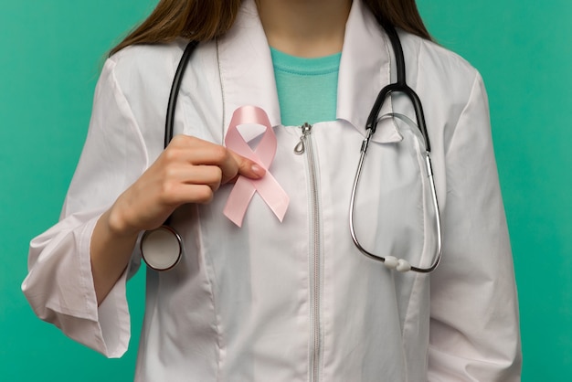 Nastro rosa per la consapevolezza del cancro al seno nella mano del medico della donna sullo spazio blu