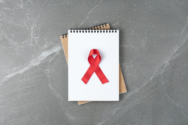 Nastro rosso di aiuto sul taccuino sul tavolo di marmo grigio, vista dall'alto. simbolo della lotta contro l'HIV e l'AIDS, piatto laici.