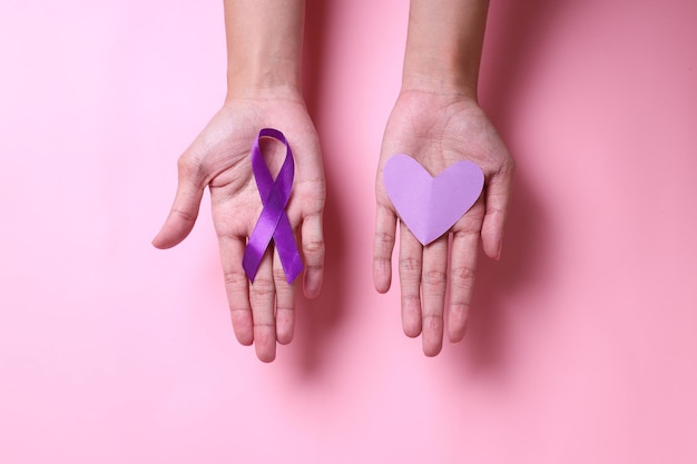 Nastro viola e forma a cuore sui palmi delle mani per sostenere la giornata mondiale dell'epilessia e la consapevolezza del cancro