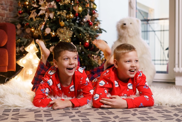 Natale a casa i bambini giacciono sotto l'albero ragazzini in pigiama rosso che celebrano le feste invernali...