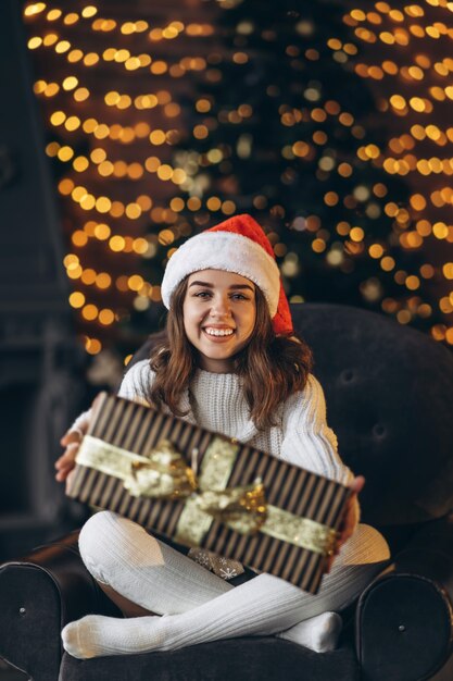 Natale, Capodanno. Bella donna in maglione caldo seduto sulla sedia a casa con confezione regalo