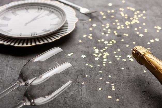 Natale, celebrazione del nuovo anno che serve un piatto a forma di orologio, bottiglie di champagne, due bicchieri di champagne e coriandoli glitter oro, T