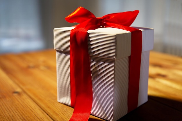 natale, compleanno, vacanze, regali e concetto di celebrazione - primo piano della confezione regalo con fiocco rosso sul tavolo di legno