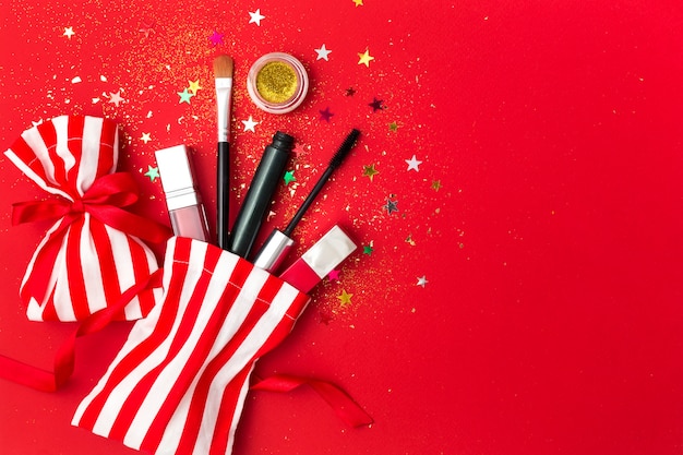 Natale con mascara, rossetto e ombre. Composizione piatta con scintillii, sacchetti regalo e prodotti cosmetici per la festa di Capodanno.