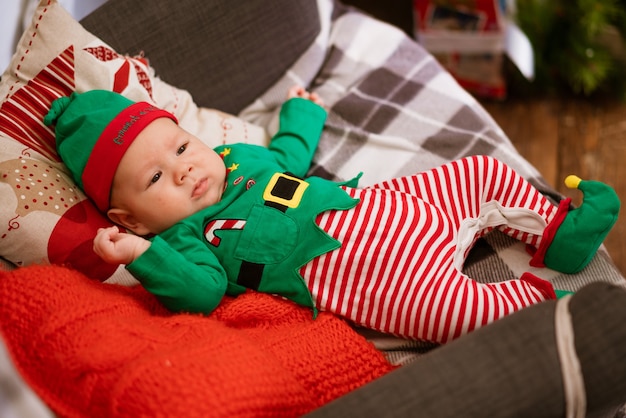 Natale concetto ragazzino allegro elfo che cerca bugie su cuscini multicolori in costume da gnomo s...