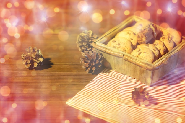 natale, cottura al forno, cucina, vacanze e concetto di cibo - primo piano di biscotti d'avena in scatola di legno con cannella e pigne sul tavolo sopra le luci