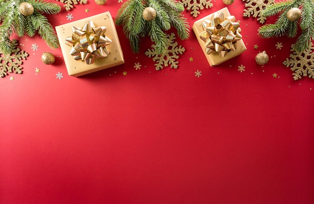 Natale e Capodanno concetto di sfondo. Vista dall'alto della decorazione natalizia realizzata con scatola regalo, fiocco di neve, palla di Natale e rami di pino su sfondo rosso.