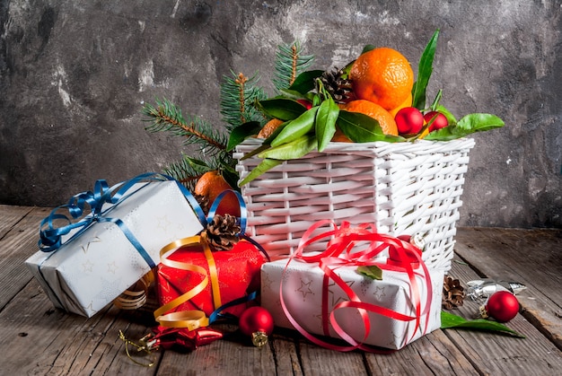 Natale e. Mandarini freschi con foglie verdi in un cestino bianco, decorazioni natalizie e scatole regalo, sul vecchio tavolo di legno rustico,