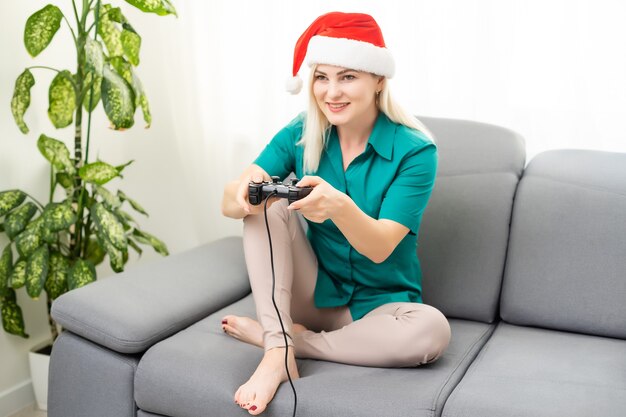 Natale, gioco, vacanza, celebrazione e concetto di tecnologia - donna che tiene in mano un gamepad e gioca ai videogiochi a casa