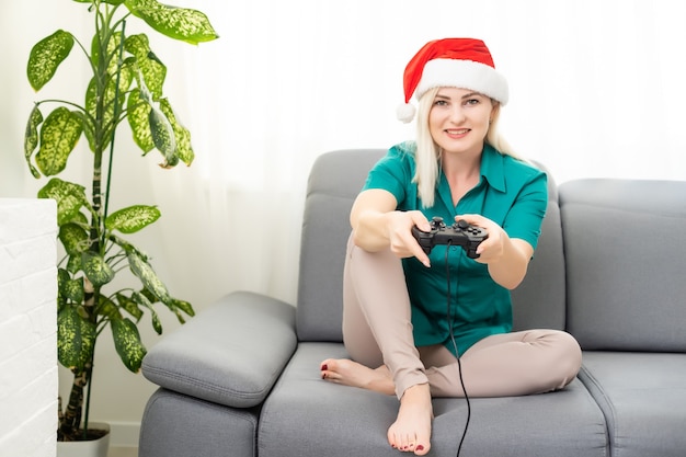 Natale, gioco, vacanza, celebrazione e concetto di tecnologia - donna che tiene in mano un gamepad e gioca ai videogiochi a casa