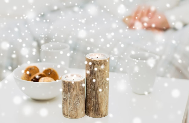 Natale, inverno, vacanze e concetto - primo piano di candele, biscotti e tazze da tè sul tavolo sopra la coppia di famiglia sullo sfondo