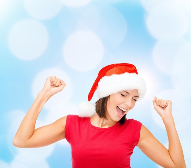 Natale, inverno, vacanze, felicità e concetto di persone - donna sorridente in cappello santa helper e camicia rossa vuota su sfondo di luci blu