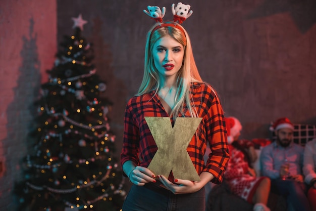 Natale, natale, capodanno, inverno, concetto di felicità - donna sorridente in cappello dell'assistente di santa con una lettera di legno X.