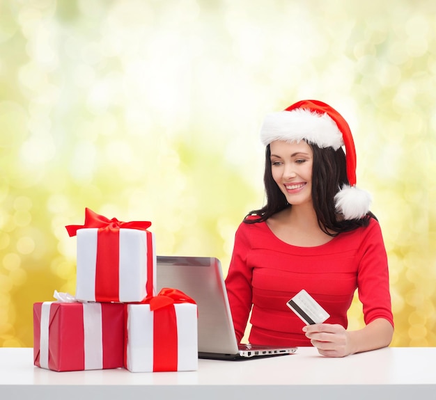 natale, natale, concetto di shopping online - donna con cappello da Babbo Natale con scatole regalo, computer portatile e carta di credito