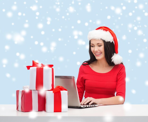 natale, natale, concetto di shopping online - donna con cappello da Babbo Natale con scatole regalo e computer portatile