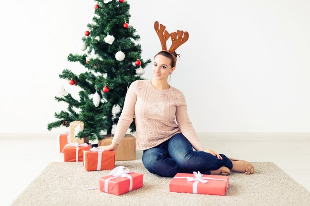 Natale, natale, inverno, concetto di felicità - la ragazza apre un regalo sullo sfondo dell'albero di Natale. Felice giovane donna che celebra il Natale