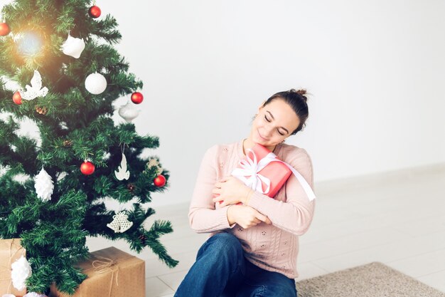 Natale, natale, inverno, concetto di felicità - la ragazza apre un regalo sullo sfondo dell'albero di Natale. Felice giovane donna che celebra il Natale