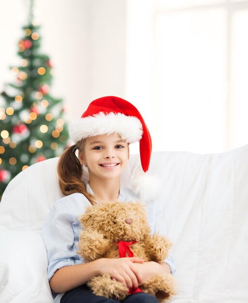 natale, natale, inverno, concetto di felicità - ragazza sorridente con cappello da Babbo Natale con orsacchiotto a casa