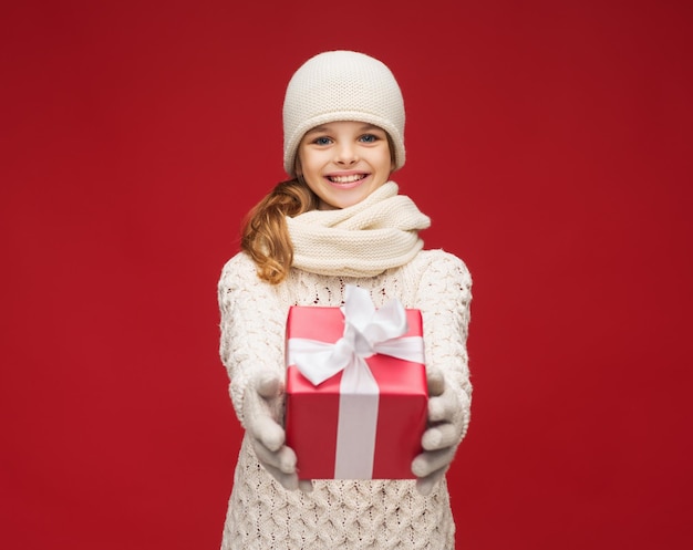 natale, natale, inverno, concetto di felicità - ragazza sorridente con cappello, sciarpa e guanti con confezione regalo