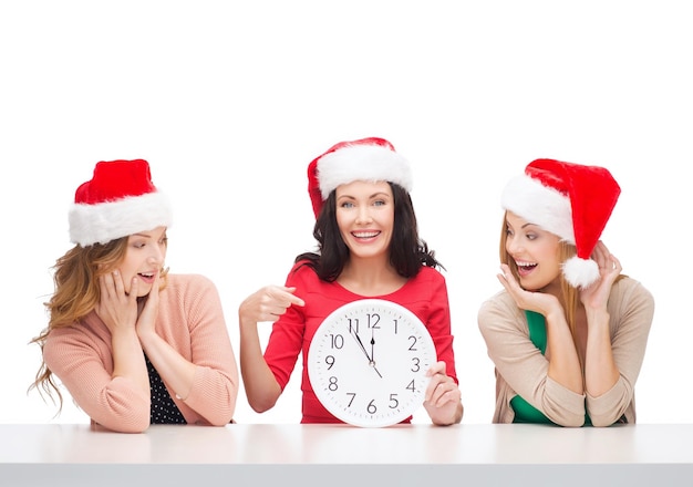 natale, natale, inverno, concetto di felicità - tre donne sorridenti in cappelli di santa helper con orologio che mostra 12