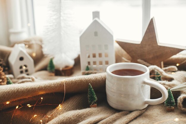 Natale natura morta inverno casa hygge Calda tazza di tè decorazioni natalizie e luci alla finestra