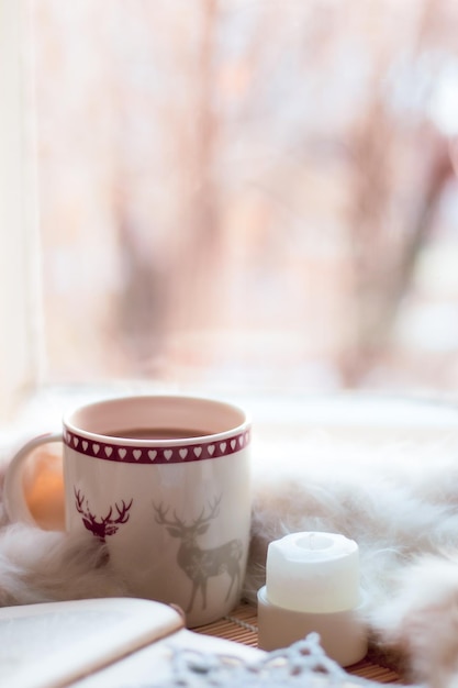 natale natura morta, tazza di cacao, libro, coperta, candela, fiocco di neve lavorato a maglia sul davanzale