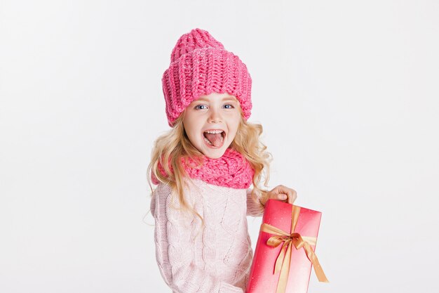 Natale. Nuovo anno. Bambina che tiene presente in abiti invernali. Cappello e sciarpa rosa. Inverno