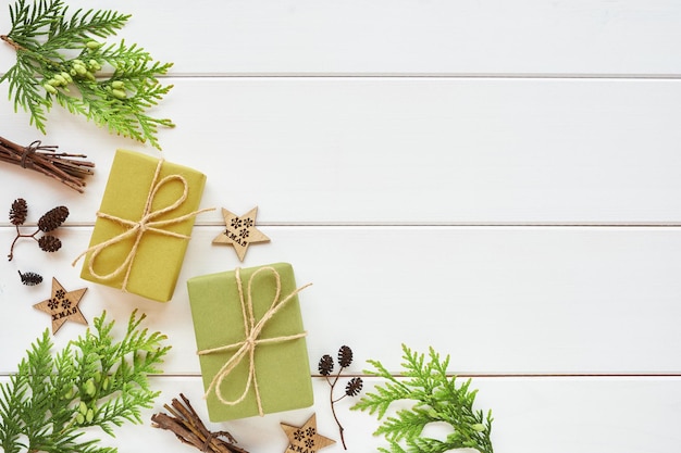 Natale o Capodanno arrangiamento. Bordo angolare realizzato con scatole regalo, rami di conifere e decorazioni naturali su fondo di legno bianco. Lay piatto, vista dall'alto, copia spazio.