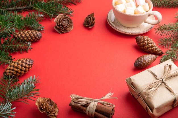 Natale o composizione. Decorazioni, scatola, cannella, coni, rami di abete e abete rosso, tazza di caffè su carta rossa.