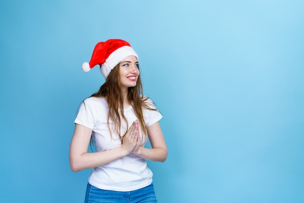 Natale santa cappello isolato ritratto di donna sorridente ragazza felice su sfondo blu in maglietta bianca per...