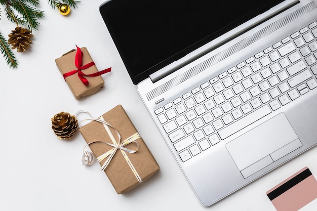 Natale shopping online laici piatta. Un laptop aperto, una carta di credito, scatole regalo legate con un nastro rosso, rami di abete verde, ghirlande di stelle