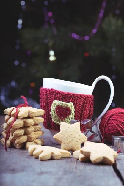 Natale - tazze di lana lavorate a maglia e pan di zenzero a forma di stella su un tavolo di legno