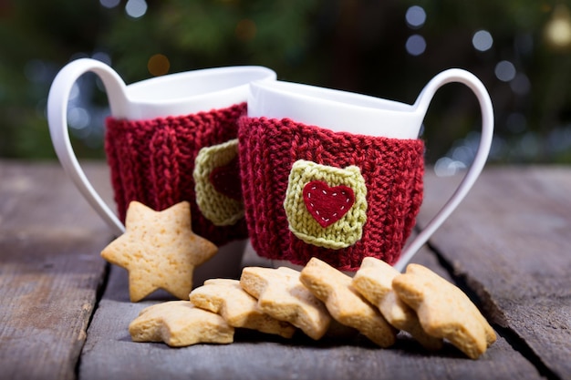Natale - tazze di lana lavorate a maglia e pan di zenzero a forma di stella su un tavolo di legno