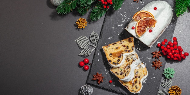 Natale tradizionale stollen Torta tedesca Pasticceria europea fragrante pane fatto in casa con spezie e frutta secca Albero di Natale rami e decorazioni sfondo nero formato banner