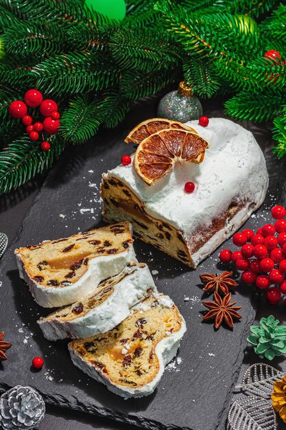 Natale tradizionale stollen Torta tedesca Pasticceria europea fragrante pane fatto in casa con spezie e frutta secca Albero di Natale rami e decorazioni sfondo nero primo piano