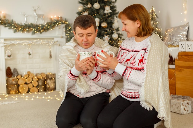 Natale, un uomo e una donna con maglioni identici, bevono il tè sotto una coperta