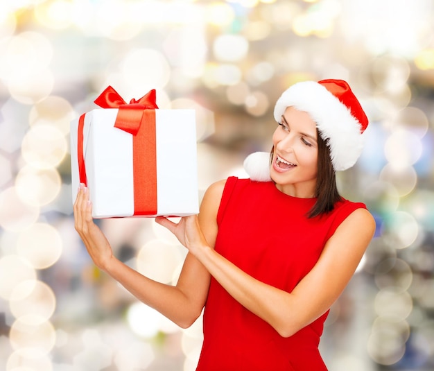 Natale, vacanze, celebrazione e concetto di persone - donna sorridente in abito rosso con confezione regalo su sfondo di luci