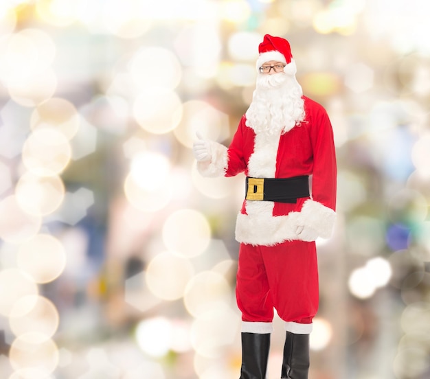 natale, vacanze, gesto e concetto di persone - uomo in costume di babbo natale che mostra i pollici in su su sfondo di luci