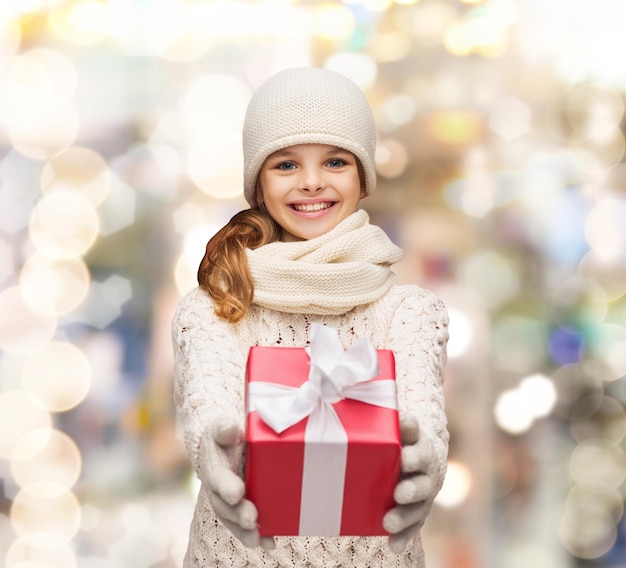 Natale, vacanze, infanzia, regali e concetto di persone - ragazza sognante in abiti invernali con confezione regalo su sfondo di luci