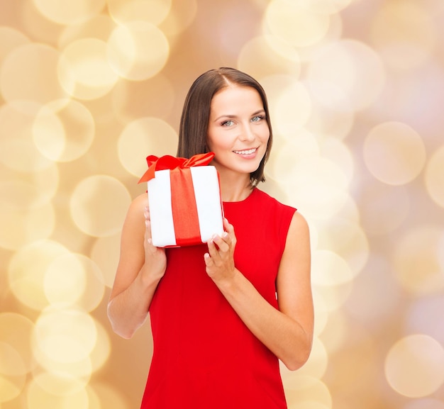 Natale, vacanze, San Valentino, celebrazione e concetto di persone - donna sorridente in abito rosso con confezione regalo su sfondo di luci beige