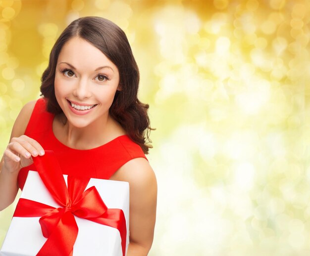 Natale, vacanze, San Valentino, celebrazione e concetto di persone - donna sorridente in abito rosso con confezione regalo su sfondo di luci gialle