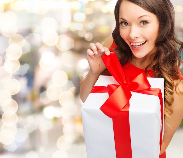 Natale, vacanze, San Valentino, celebrazione e concetto di persone - donna sorridente in abito rosso con confezione regalo su sfondo di luci