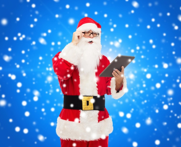 Natale, vacanze, tecnologia e concetto di persone - uomo in costume di babbo natale con computer tablet pc su sfondo blu innevato