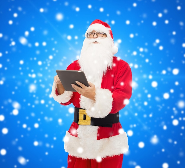 Natale, vacanze, tecnologia e concetto di persone - uomo in costume di babbo natale con computer tablet pc su sfondo blu innevato