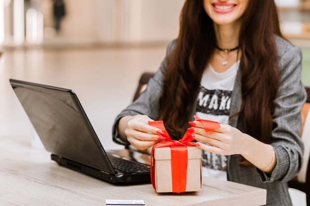 Natale, vacanze, tecnologia e concetto di shopping - donna sorridente con carta di credito sul tavolo, confezione regalo e computer portatile. Foto orizzontale